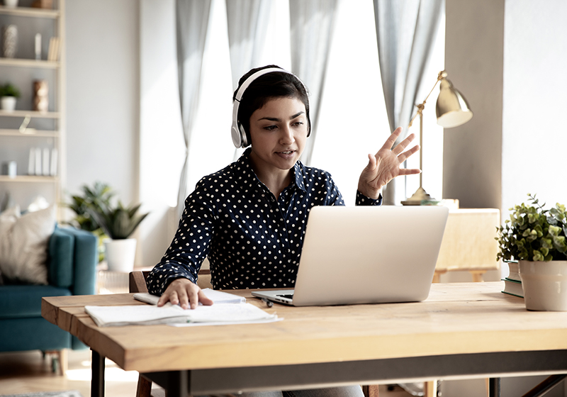 En kvinna sitter vid ett skrivbord framför sin laptop med hörlurar på