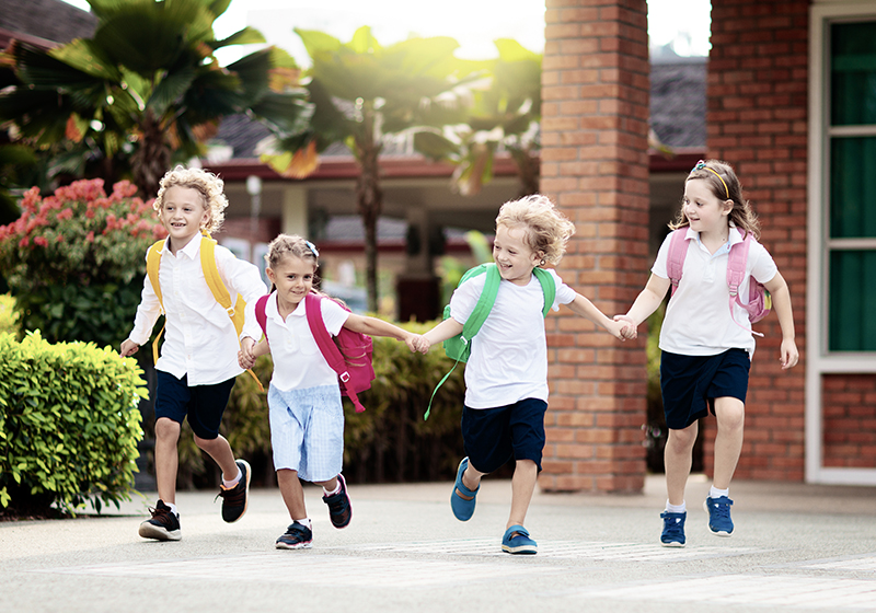 Fyra barn håller hand och springer leendes mot kameran